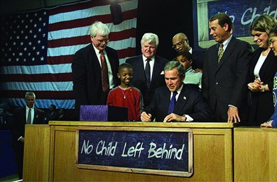A photograph shows President Bush signing the No Child Left Behind Act at a large desk, surrounded by U.S. officials and several children. On the desk hangs a chalkboard that reads “No Child Left Behind.”