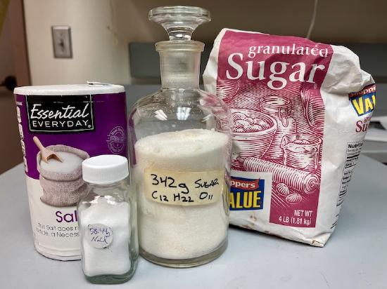 Image of one mole of table salt (58.44 grams) and one mole of sugar (342 grams).