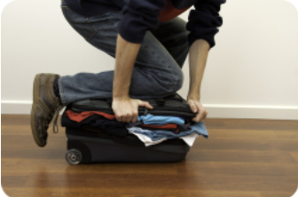 Una persona que intenta cerrar su maleta poniendo su rodilla en la maleta.