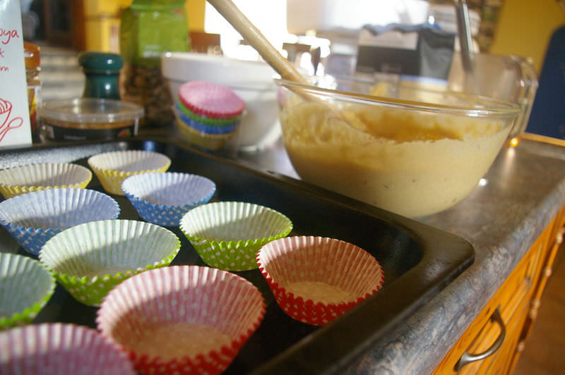 Cupcake batter next to a pan with empty cupcake wrappers on a kitchen counter.