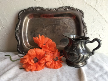 Bandeja para servir antigua y jarra con tres flores anaranjadas contra una sábana blanca.