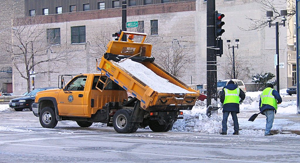 Workers spreading salt from a salt truck onto the road.