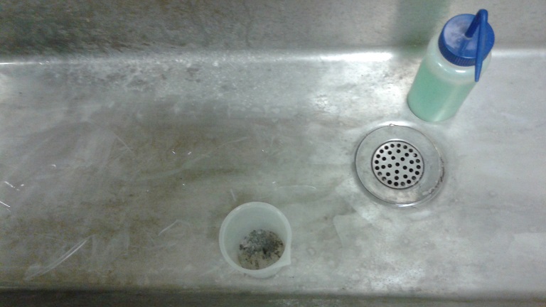 Un lavabo, con detergente en una botella de chorro y la muestra en una taza para lavar (tamiz no representado).