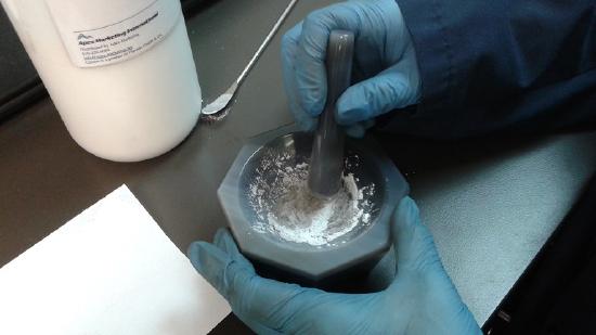A mortar and pestle being used to grind the sample to a powder for pelleting in the pellet press. A binding agent (Cereox) is also added using the scapula.
