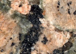 Close-up of granite shows areas of white, salmon, and grey rock and areas of black graphite