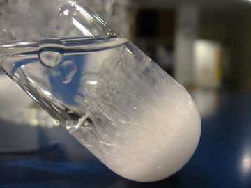 Test tube with crystals at the bottom and along the glass; Viscous transparent liquid on top.