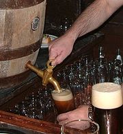 Picture of a hand operating a beer barrel tap to pour a glass of beer.