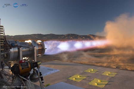 Grandes llamas salen del cohete en una trayectoria horizontal. El cohete y el motor están en una instalación de pruebas.