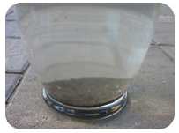 A clear glass filled with water, showing sediment settled at the bottom, placed on a concrete surface outdoors.