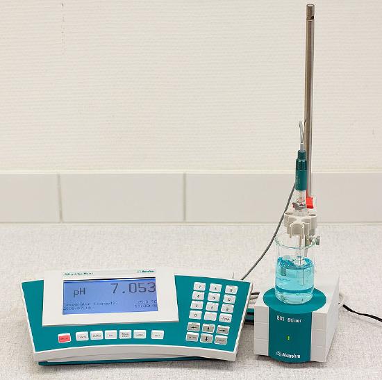 Image of a pH meter testing the pH of a solution in a glass beaker. The meter shows a reading of pH 7.053.