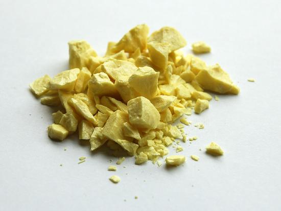 Chunks of sulphur are stacked on a while surface.