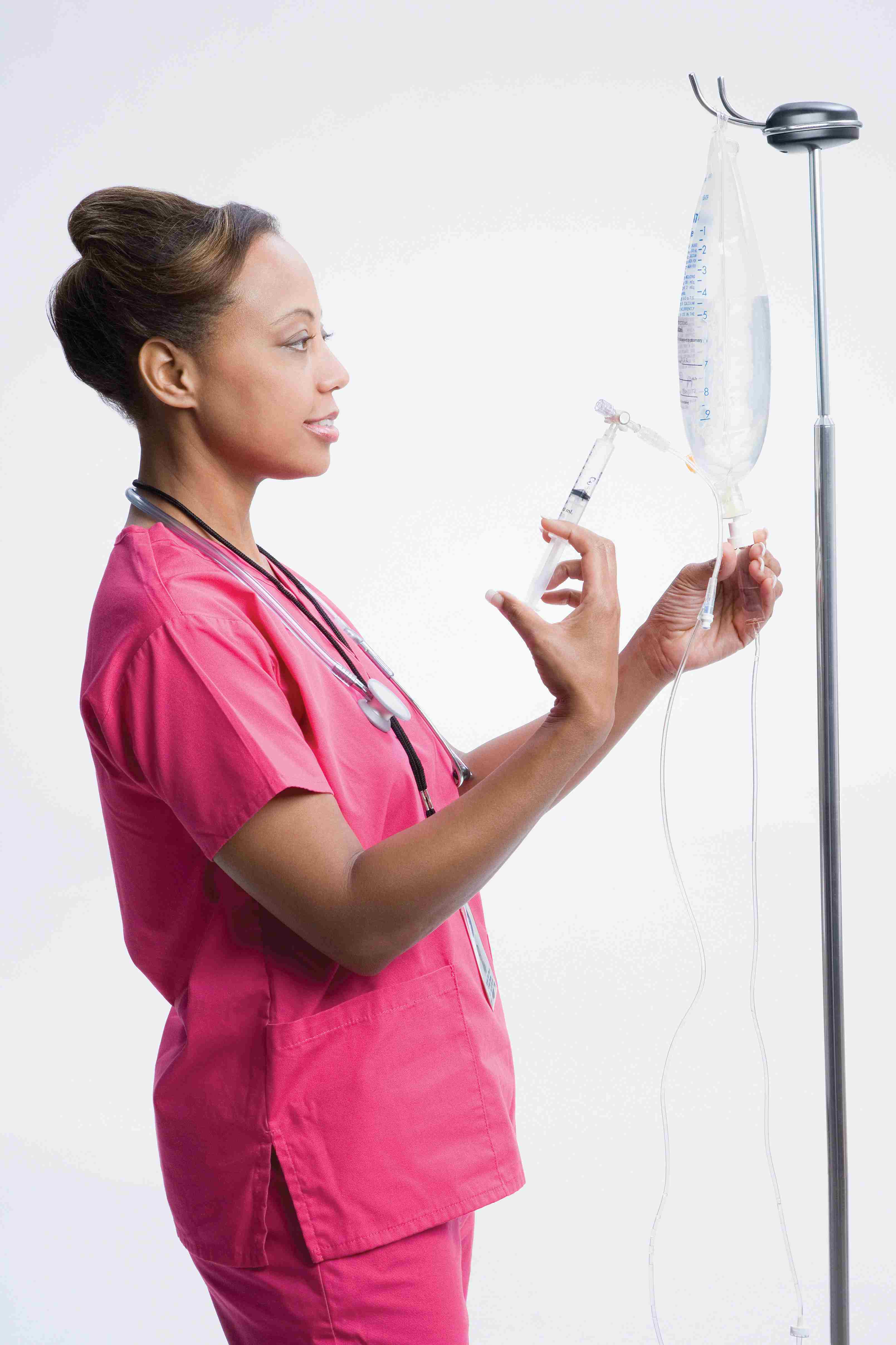 Una enfermera en matorrales rosados usa una jeringa para preparar una solución IV.