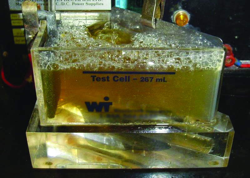 Metales en un líquido de color amarillo dentro de un recipiente, los metales están siendo galvanoplastia.
